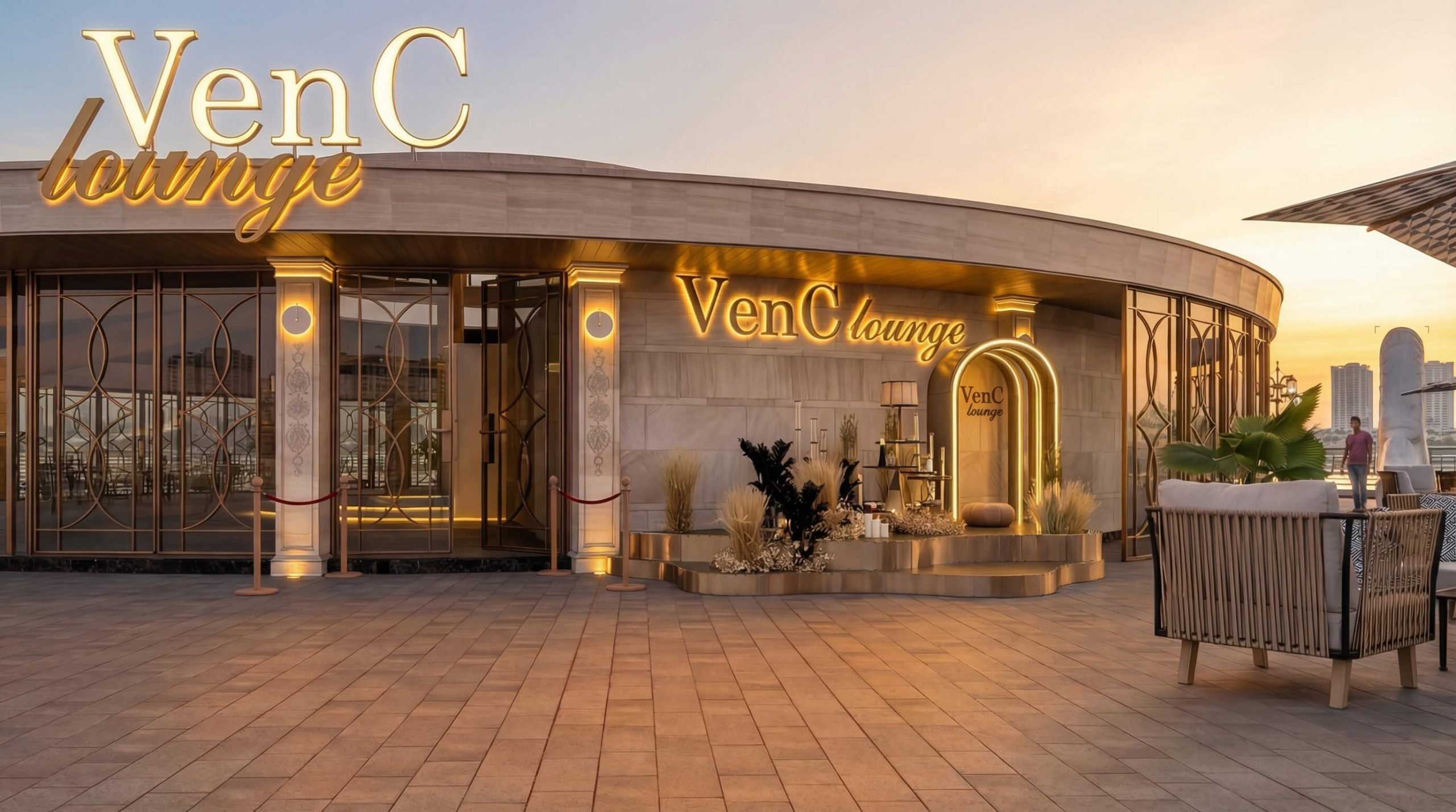 Hình ảnh VenC Lounge với thiết kế rooftop hiện đại, nổi bật với hệ thống ánh sáng vàng sang trọng và kiến trúc đường cong mềm mại. Không gian được bố trí tinh tế với khu vực tiếp khách ngoài trời, cửa kính trang trí họa tiết nghệ thuật và khu check-in đẳng cấp. Đây là điểm đến lý tưởng cho trải nghiệm lounge cao cấp, thư giãn và ngắm cảnh thành phố vào hoàng hôn.